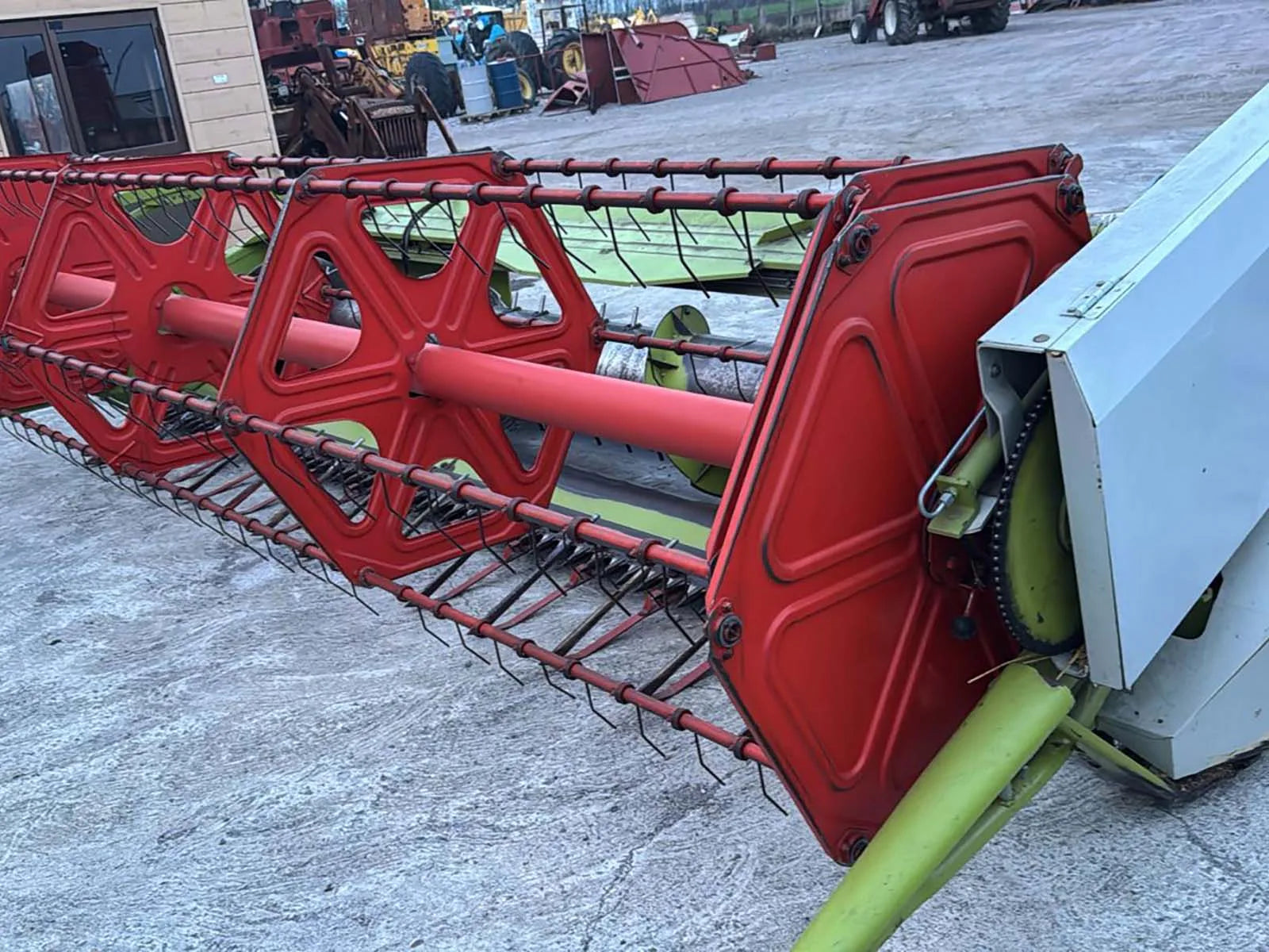Red agricultural header attached to a vehicle on a concrete surface