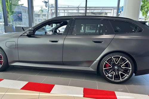 Gray car on display inside a showroom with a red and white striped barrier.