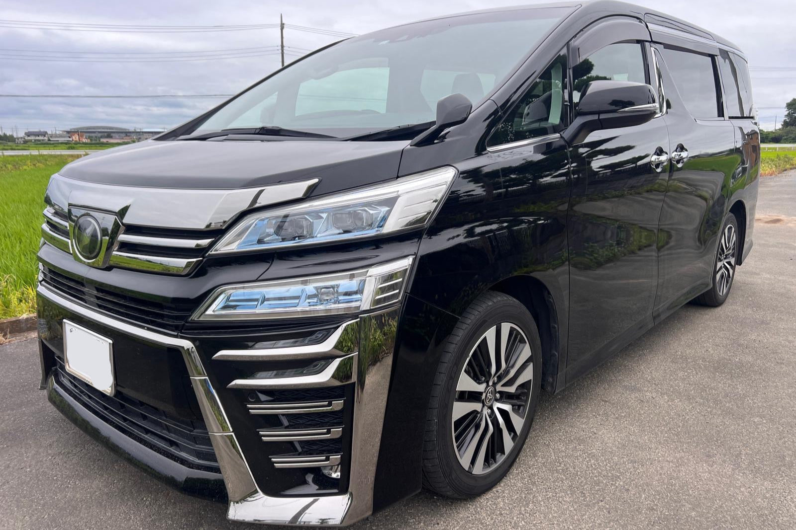 Black Toyota minivan parked on a road with a rural landscape in the background
