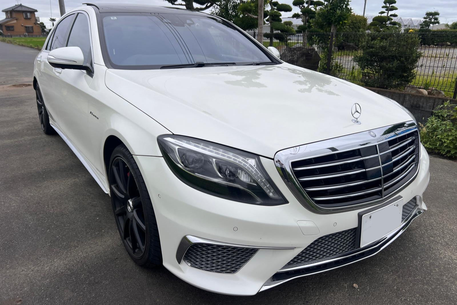 White Mercedes-Benz car parked on a road with a garden in the background