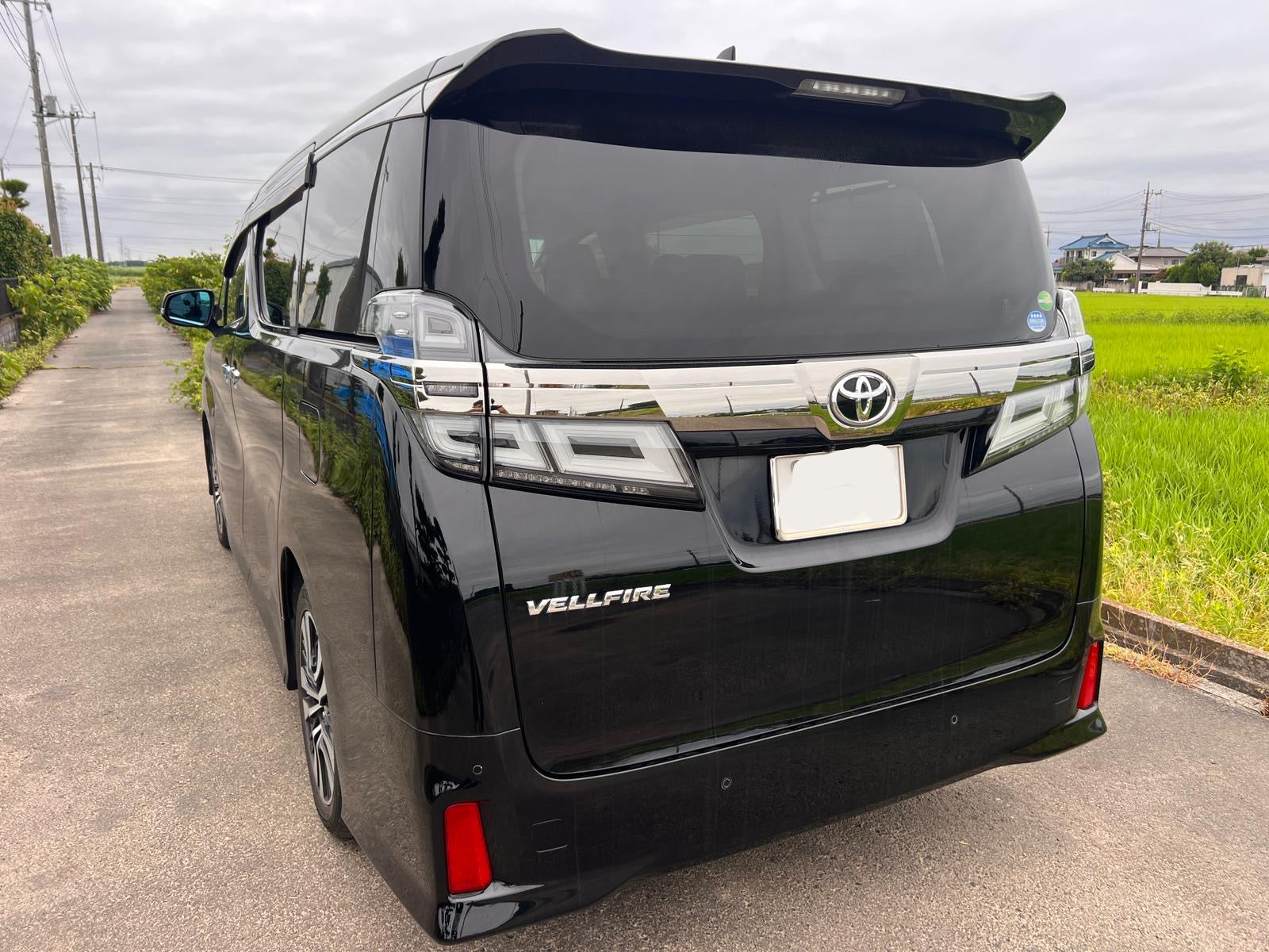 Black Toyota Vellfire minivan on a road with greenery in the background