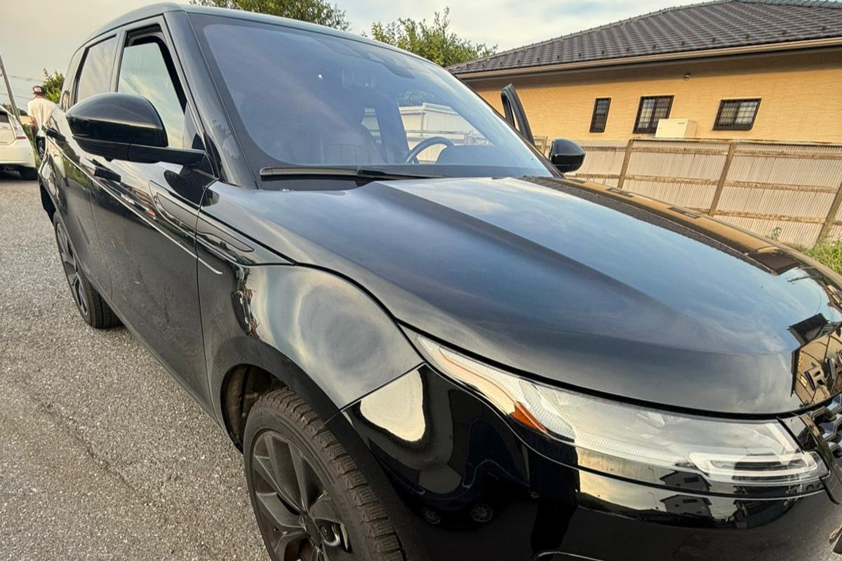 Black car parked on a street with a house in the background