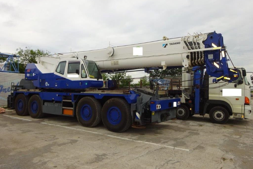 Blue and white crane truck on a concrete surface with a cloudy sky.